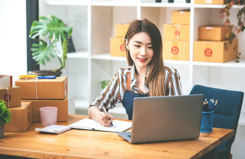Une femme sur un ordinateur avec des colis posés sur la table à coté